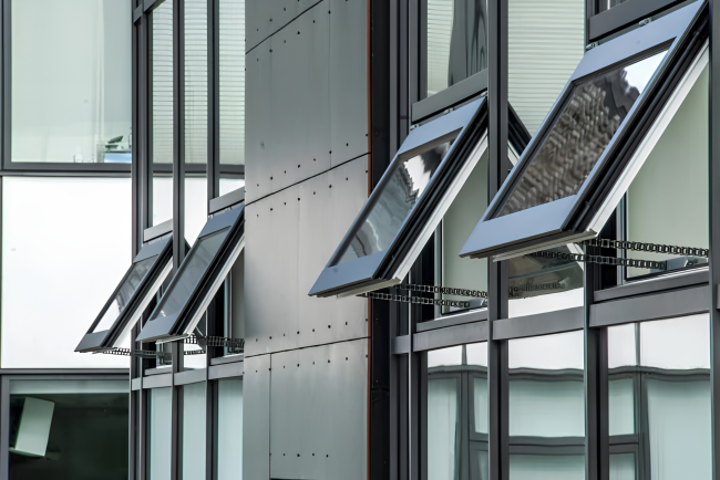 Row of automatic opening vents with chain actuators, open on the glazed facade of a building