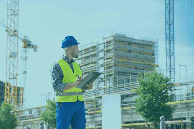 Clerk of Works reviewing inspection notes on a clipboard in front of a high-rise building under construction, illustrating independent site inspection during new-build residential construction.