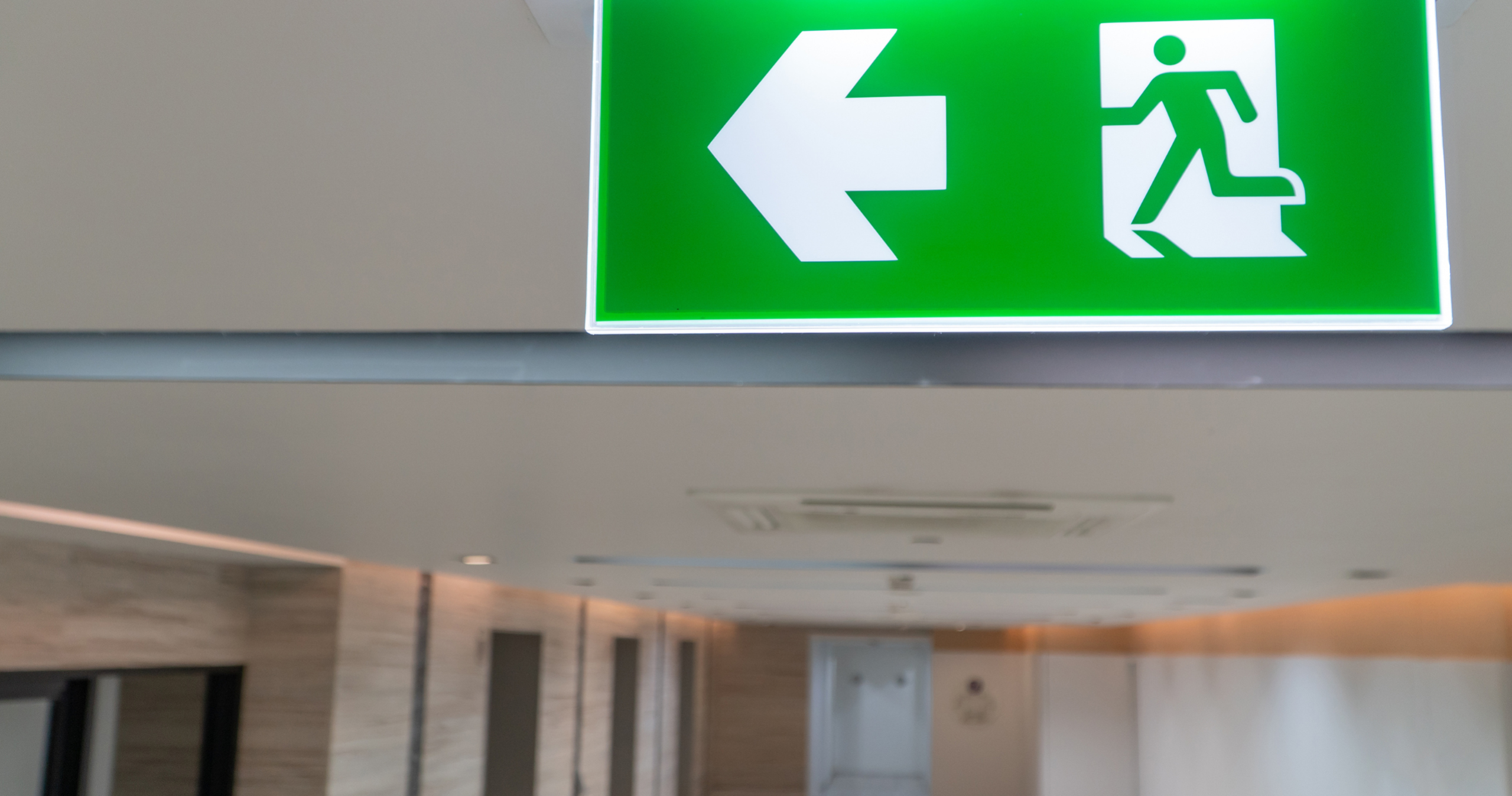 DALA Blog -Fire Enforcement Notice Illuminated green fire exit sign with a left-pointing arrow above a corridor in a building
