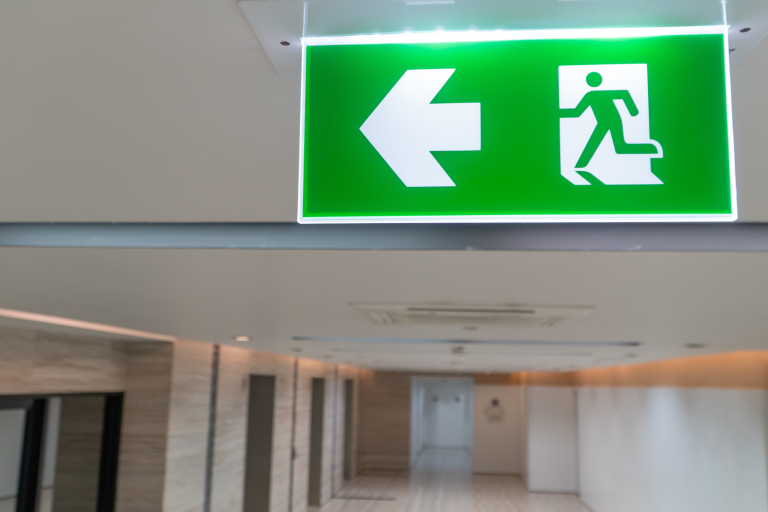 Illuminated green fire exit sign with a left-pointing arrow above a corridor in a building