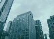 Looking up at glass-fronted high-rise buildings against an overcast sky.