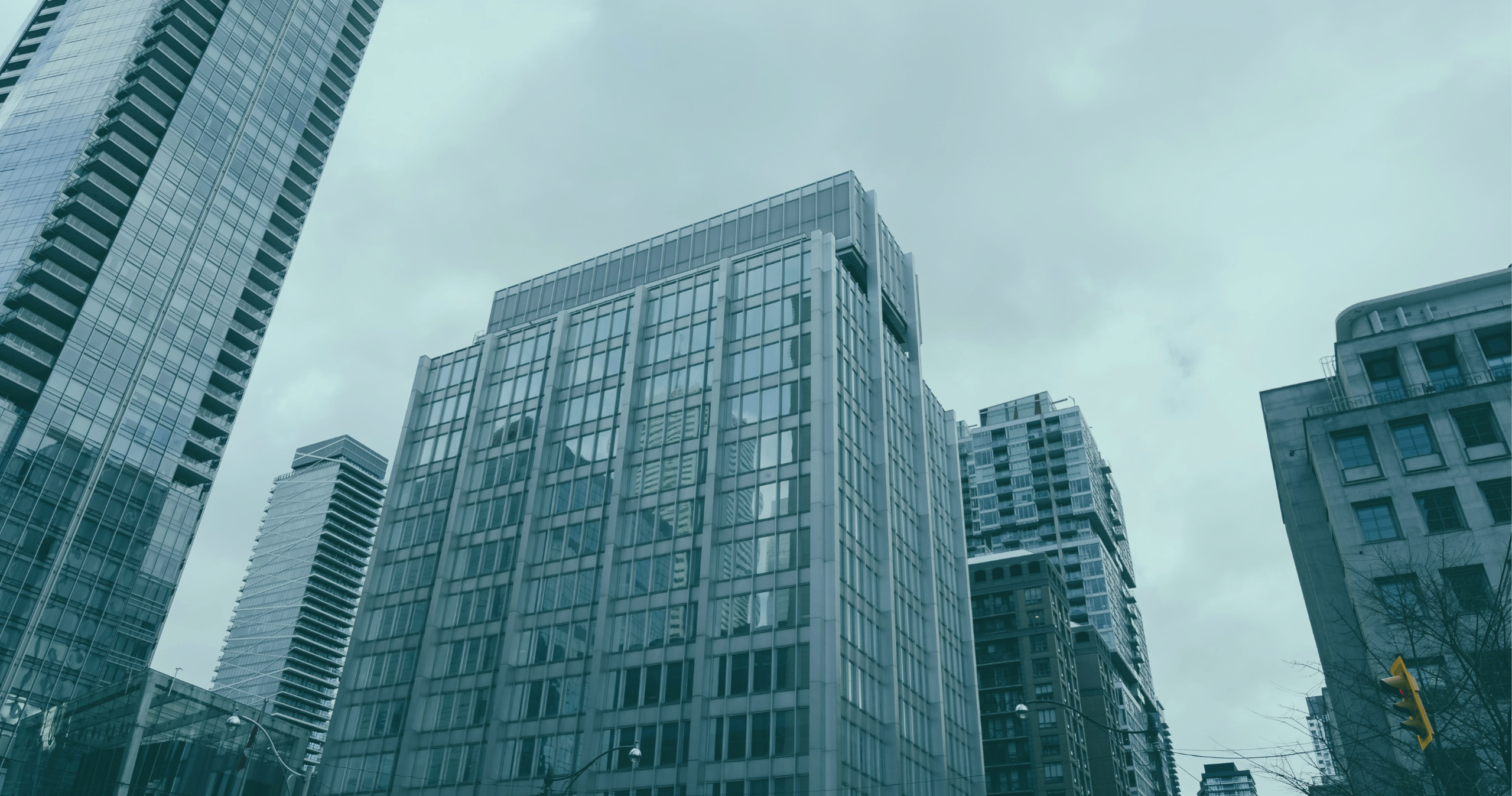 Looking up at glass-fronted high-rise buildings against an overcast sky.