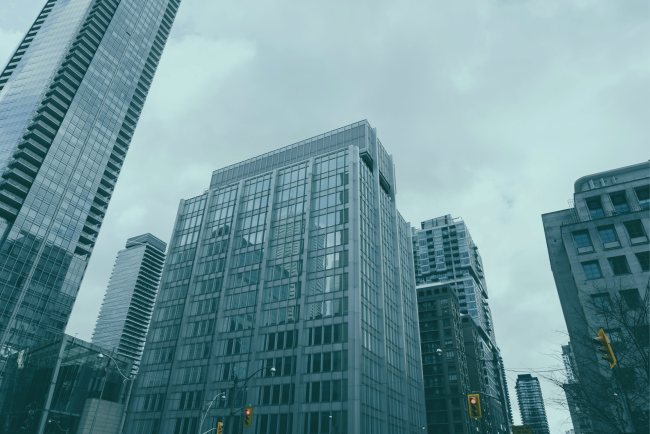 Multi-storey residential and commercial buildings in an urban setting Looking up at glass-fronted high-rise buildings against an overcast sky.